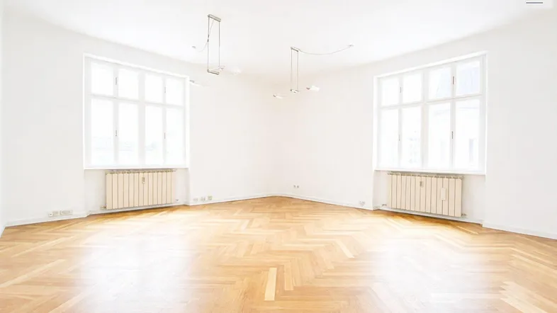 Heller, leerer Wohnraum mit Fischgrätparkett, zwei großen Fenstern und viel natürlichem Licht.