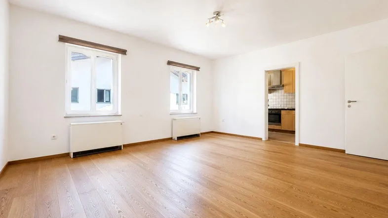 Helles Zimmer mit Holzboden und Blick in die Küche, ideal als Wohn- oder Essbereich.