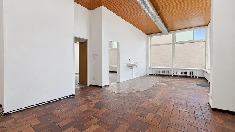 Großer, offener Gewerberaum mit Terrakottafliesen, Holzdecke und sichtbaren Lüftungsrohren, hell durch große Fenster.