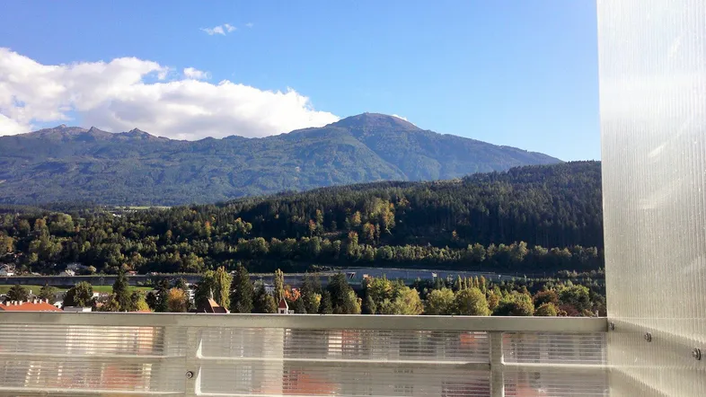 Panoramablick auf die majestätischen Berge und grüne Wälder von einem sonnigen Balkon aus.