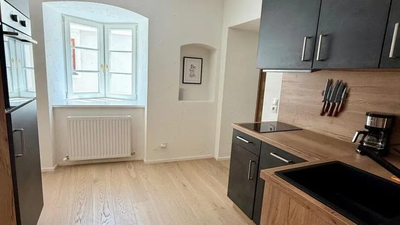 Moderne Küche mit hellen Holzelementen, dunklen Arbeitsplatten und einem Fenster für Tageslicht.
