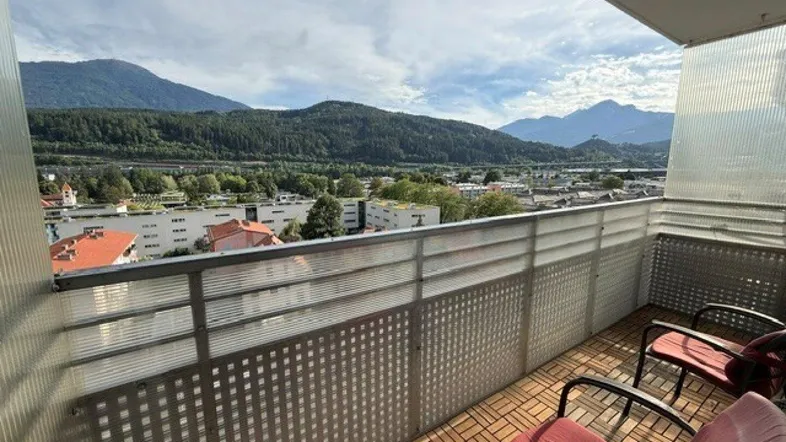 Geräumiger Balkon mit Holzboden und bequemen Stühlen, bietet einen weiten Blick auf die Stadt und die Berge.