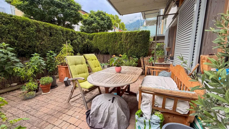Gemütliche Terrasse mit Gartenmöbeln, umgeben von einer grünen Hecke und Pflanzen.