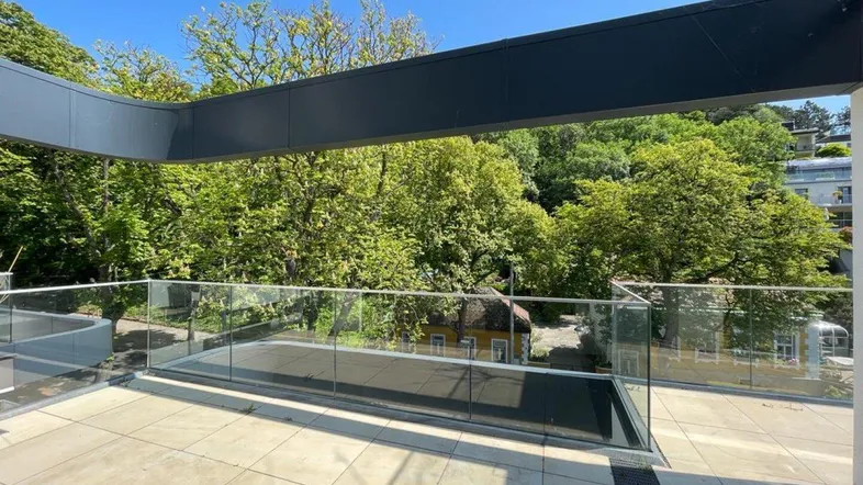 Geräumige Terrasse mit Glasgeländer und weitem Blick ins Grüne, ideal zum Entspannen im Freien.