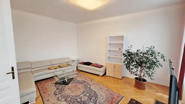 Gemütliches Wohnzimmer mit großem L-Sofa, Teppich und klassischem Fischgrätparkettboden.