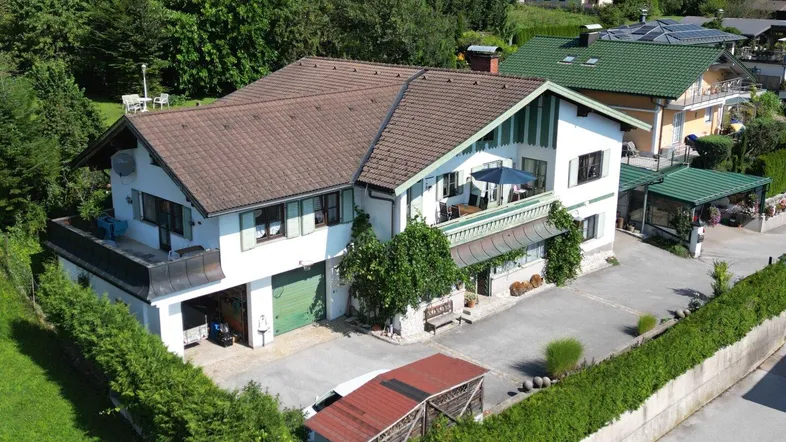 Luftaufnahme eines traditionellen Hauses mit braunem Dach, grünen Fensterläden und viel Grünfläche.