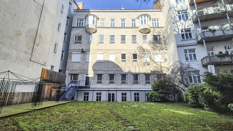 Hinteransicht eines Mehrfamilienhauses mit begrüntem Innenhof und mehreren Balkonen unter blauem Himmel.