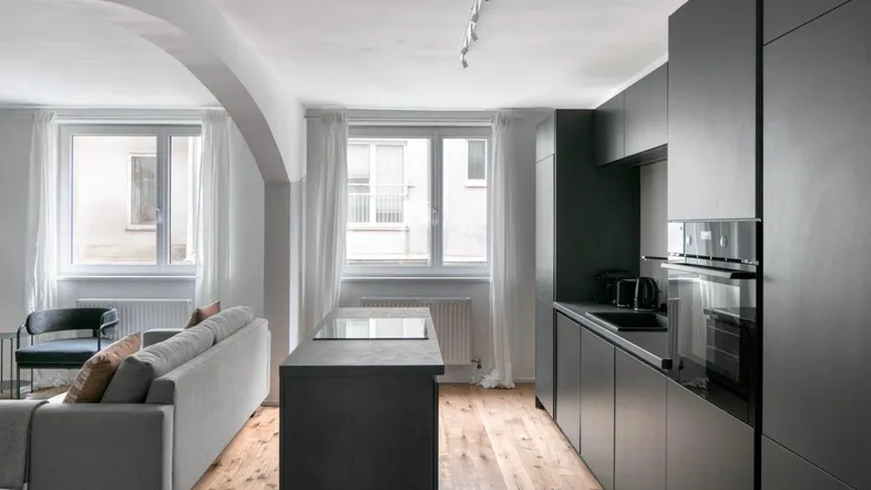 Moderne offene Küche mit dunklen Schränken und angrenzendem Wohnbereich mit Holzboden und großen Fenstern.