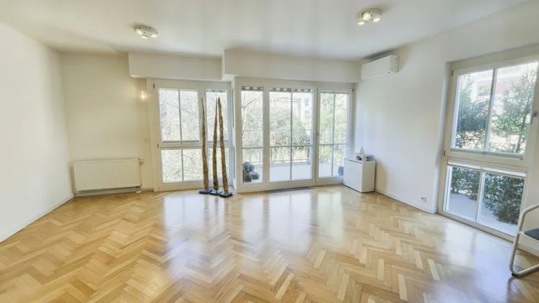Helles Wohnzimmer mit Fischgrätparkett, großen Fenstern und Zugang zu einem Balkon.