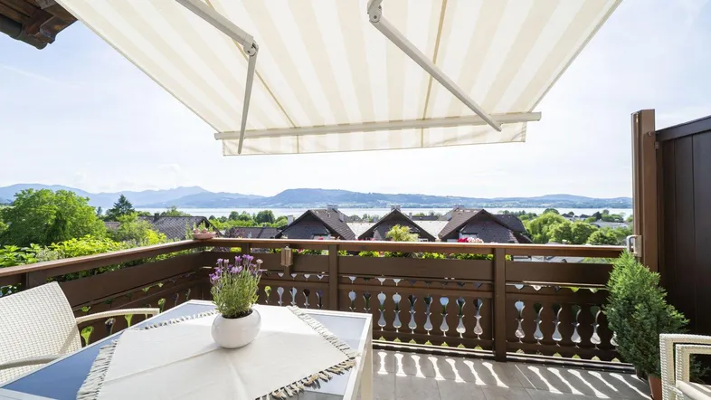 Heller Balkon mit Markise, Esstisch und weitem Blick auf den See und die Berge.