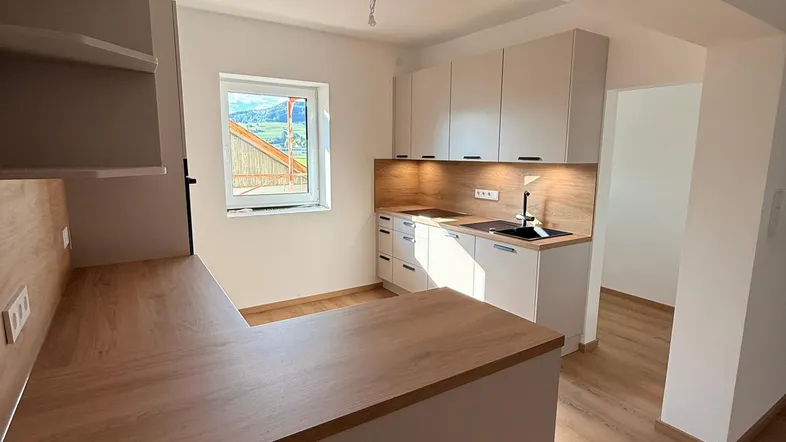 Moderne Küche mit hellen Schränken, Holzoptik-Arbeitsplatten und einem Fenster mit Blick ins Grüne.