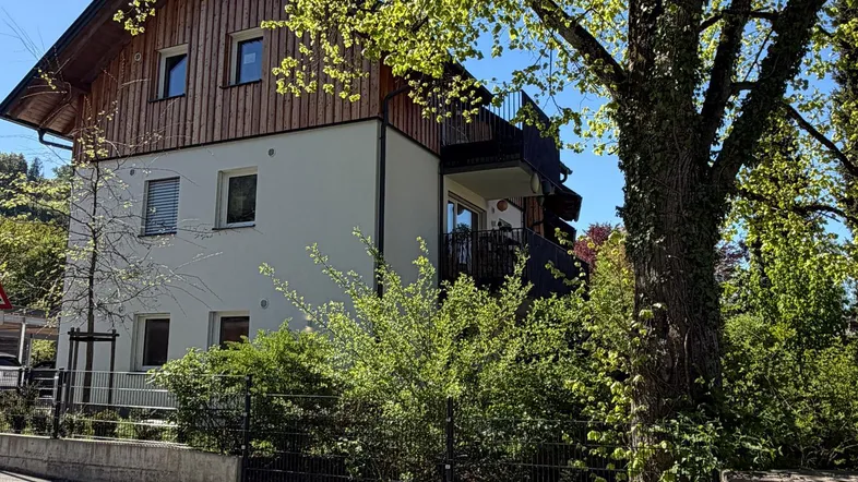 Modernes Mehrfamilienhaus mit Holzverkleidung und Balkonen, umgeben von Bäumen und Grünflächen.