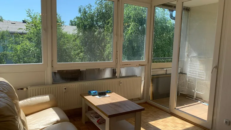 Helles Wohnzimmer mit großen Fenstern, Parkettboden und Zugang zum Balkon.