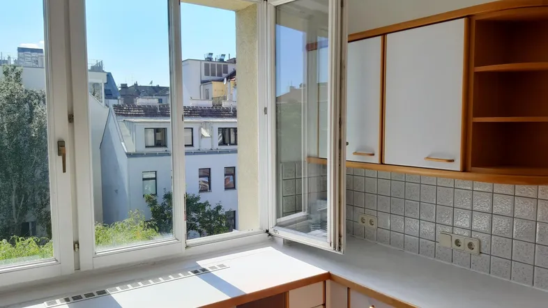 Helle Küche mit Arbeitsplatte am Fenster, Blick auf die Stadt und Oberbauschränken.