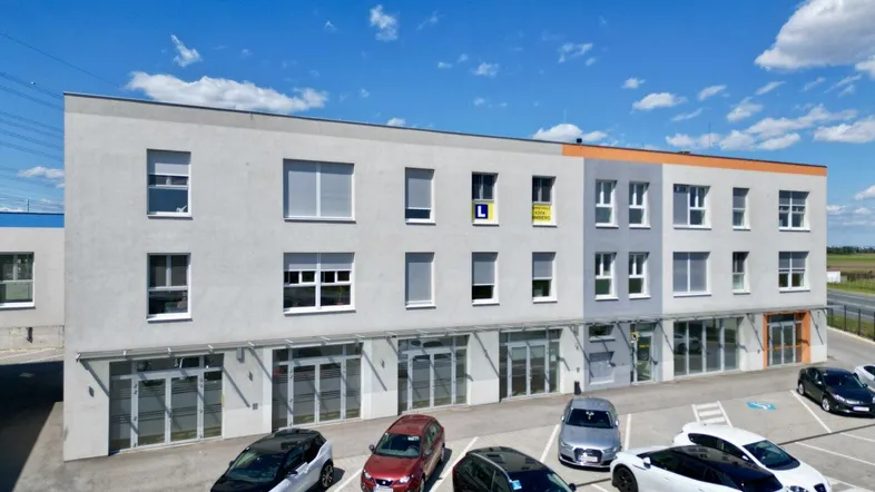 Modernes Geschäftsgebäude mit mehreren Etagen und ausreichend Parkplätzen unter blauem Himmel.