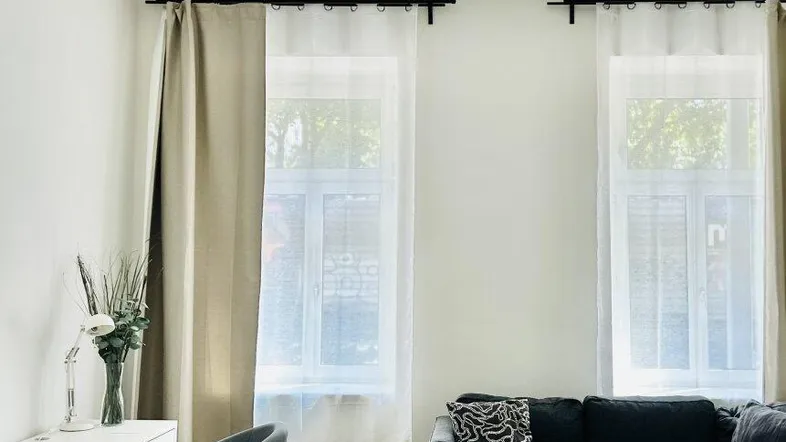Helles Wohnzimmer mit Holzboden, beigem Sofa und einem Arbeitsbereich am Fenster.