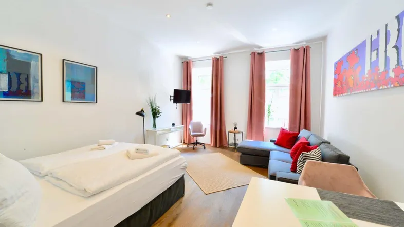 Heller Wohn- und Schlafbereich mit modernem Sofa, Esstisch und bequemen Bett.