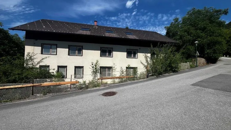 Ansicht des Gebäudes von der Straße aus mit weißer Fassade und Satteldach.