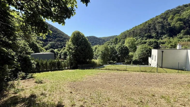 Weitläufiges Grundstück mit Blick auf bewaldete Hügel und moderne Architektur in der Ferne.
