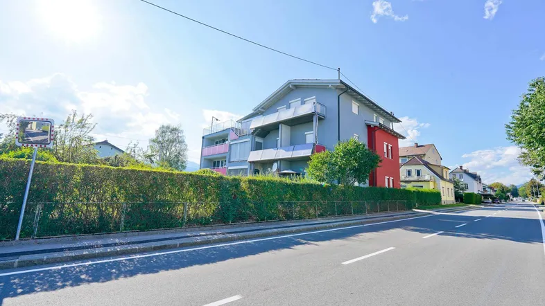 Mehrfamilienhaus mit grauer Fassade und roten Akzenten an einer Straße gelegen.