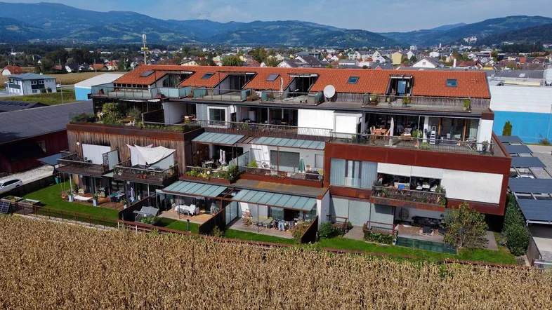 Mehrfamilienhaus-Komplex mit Terrassen, Balkonen und Blick auf die umliegende Landschaft und Berge.