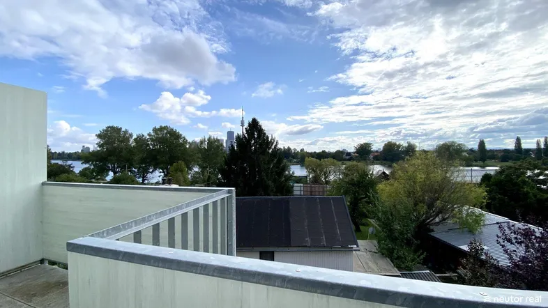Geräumiger Balkon mit weitem Blick über den See und die Stadt am Horizont unter blauem Himmel.