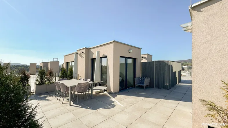 Geräumige Dachterrasse mit Sitzgelegenheiten und Pflanzen, ideal für Entspannung im Freien unter blauem Himmel.
