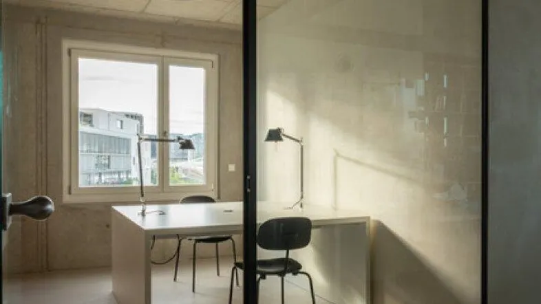 Modernes Büro mit Glasabtrennung, Schreibtischen und Blick nach draußen durch große Fenster.