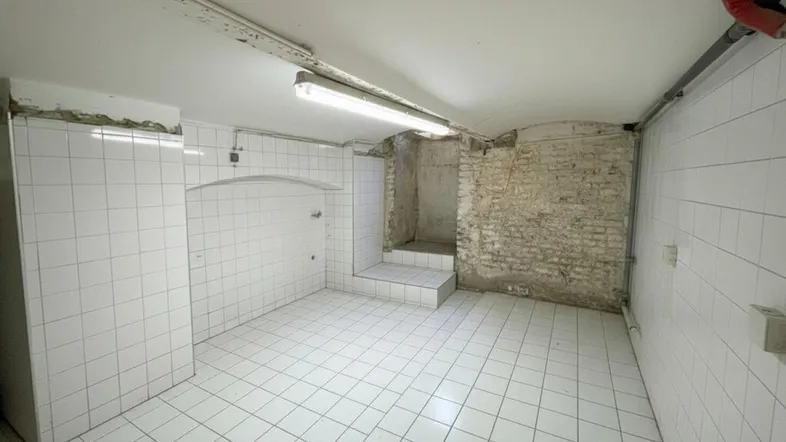 Geräumiger Kellerraum mit Fliesenboden und unverputzten Ziegelwänden, in sanierungsbedürftigem Zustand.
