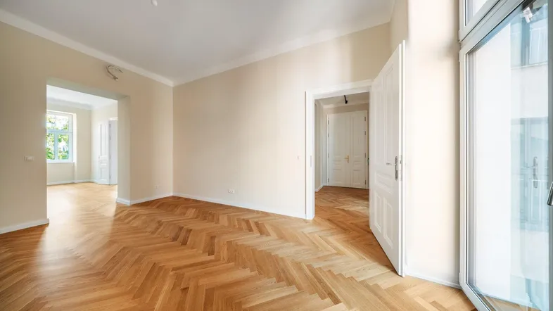 Helles Zimmer mit Fischgrätparkettboden und Zugang zu einem Balkon oder einer Terrasse.