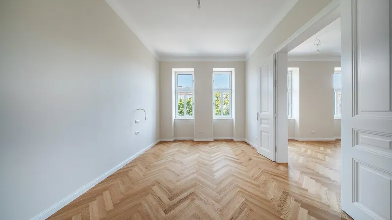 Helles, leeres Zimmer mit Fischgrätparkett und zwei Fenstern, bereit zur individuellen Gestaltung.