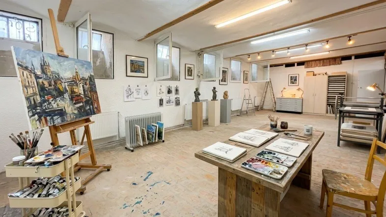 Geräumiges Kunststudio mit Staffelei, Arbeitstischen und natürlichem Licht durch mehrere Fenster.