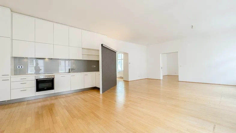 Moderne offene Küche mit weißen Hochglanzfronten und hellem Parkettboden in einem geräumigen Wohnbereich.