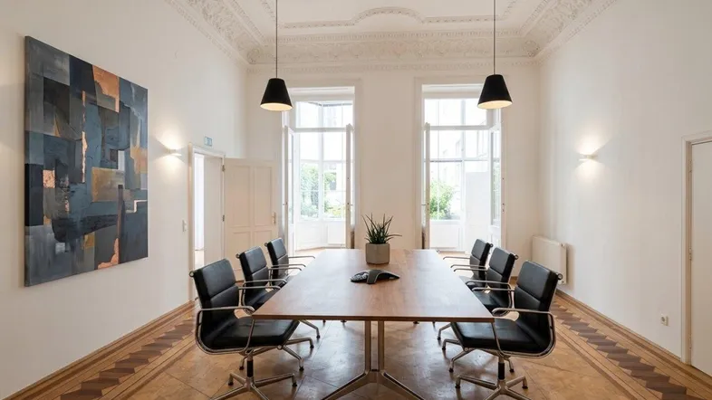 Großer Konferenzraum mit elegantem Parkettboden, Stuckdecke und Blick ins Grüne durch hohe Fenster.