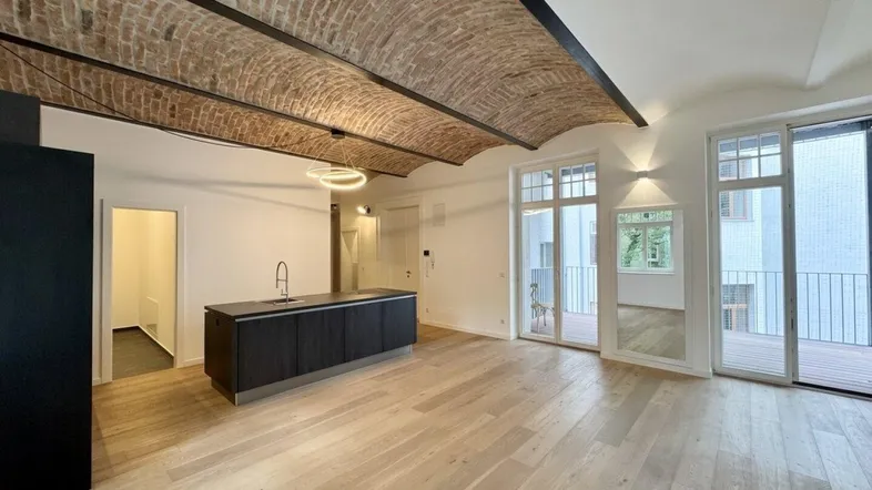 Offener Wohnbereich mit moderner Kücheninsel, Holzboden und beeindruckender Ziegelgewölbedecke.