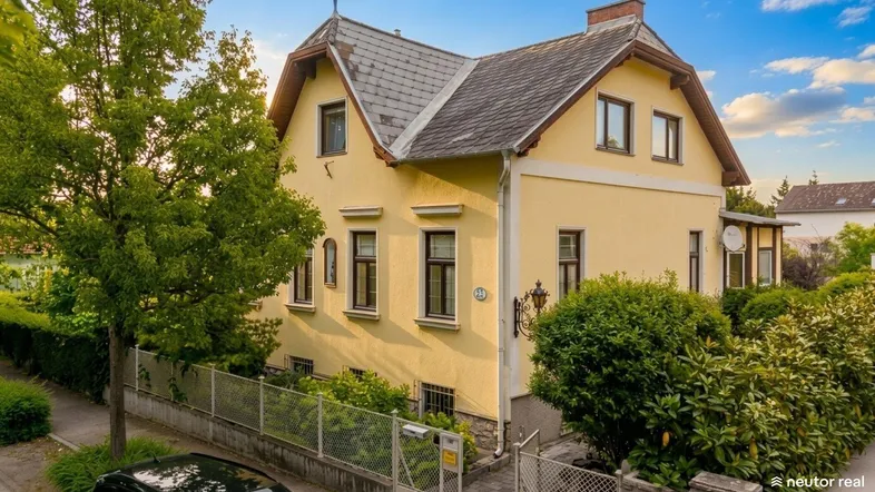Gelbes Einfamilienhaus mit traditioneller Architektur, Satteldach und gepflegtem Vorgarten unter blauem Himmel.