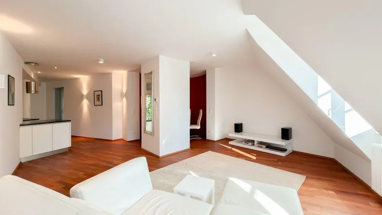Helles Dachgeschoss-Wohnzimmer mit Holzboden, weißem Sofa und offener Küchenzeile.