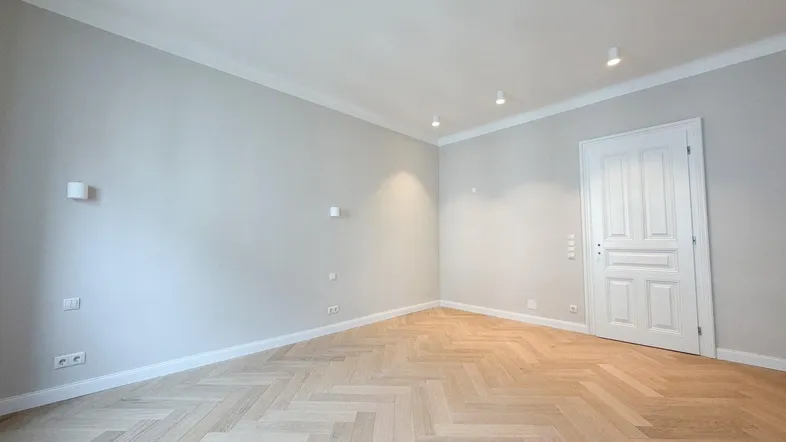 Helles Zimmer mit Fischgrätparkett, hellgrauen Wänden und einer eleganten weißen Tür.