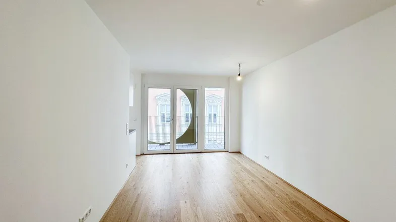 Helles Zimmer mit Parkettboden und Zugang zu einem Balkon, ideal als Wohnbereich nutzbar.