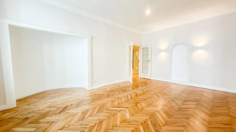 Helles Wohnzimmer mit Fischgrätparkett, hohen Decken und dekorativer Stuckrosette an der Decke.