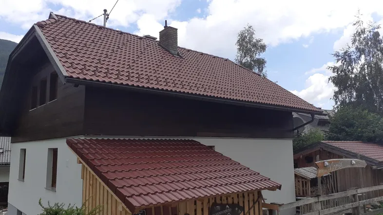 Traditionelles Haus mit rotem Ziegeldach und Holzverkleidung, umgeben von grüner Landschaft.