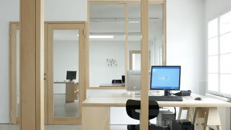 Helles und modernes Büro mit mehreren Arbeitsplätzen, Computern und Trennwänden aus Holz und Glas.