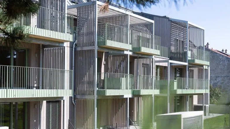Moderne Wohnanlage mit Balkonen und grünen Akzenten, umgeben von gepflegten Grünflächen.