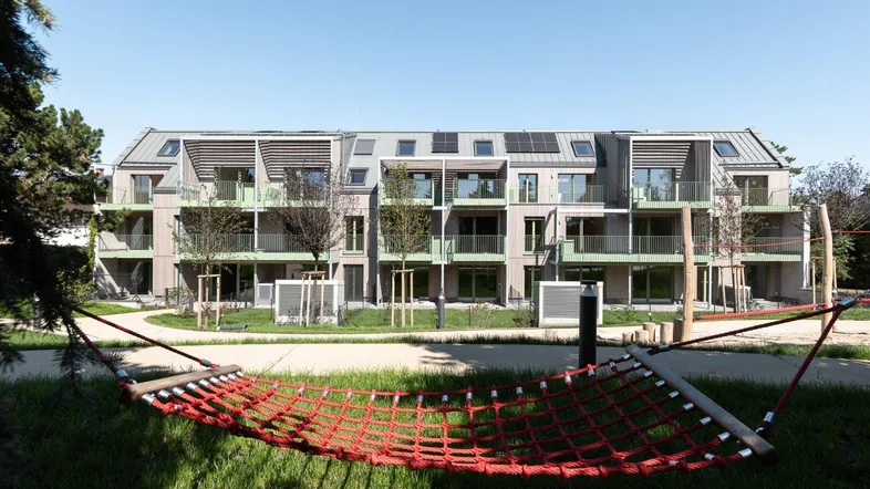 Modernes Mehrfamilienhaus mit Balkonen, Solaranlagen und einem grünen Außenbereich mit Hängematte.