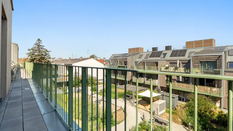 Langer Balkon mit Fliesenboden und grünem Geländer, bietet Blick auf die umliegende Wohnanlage und Grünflächen.