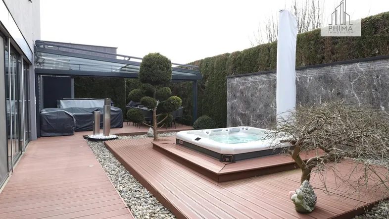 Moderne Terrasse mit integriertem Whirlpool, Holzdeck und überdachtem Sitzbereich, umgeben von einer grünen Hecke.