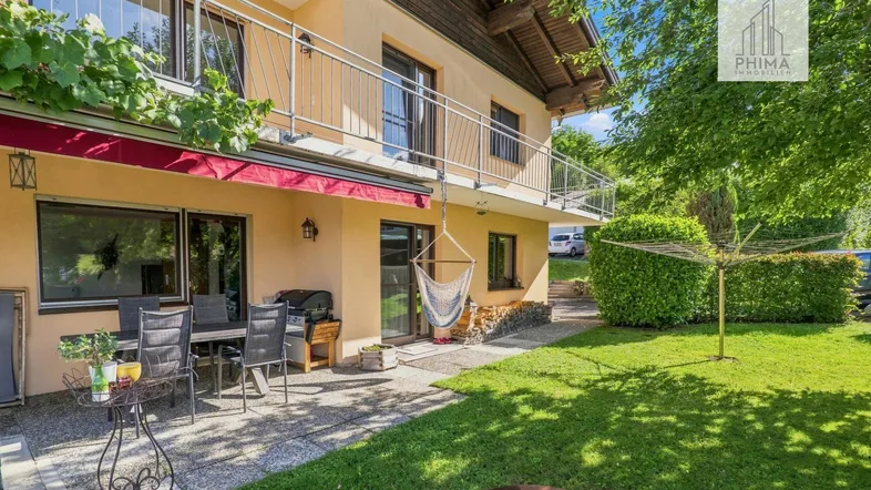 Große Terrasse mit Gartenmöbeln und Grillbereich, umgeben von einem gepflegten Rasen und Bäumen.