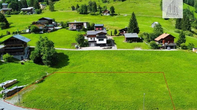 Luftaufnahme eines grünen Baugrundstücks mit roter Umrandung, umgeben von Häusern und Natur.
