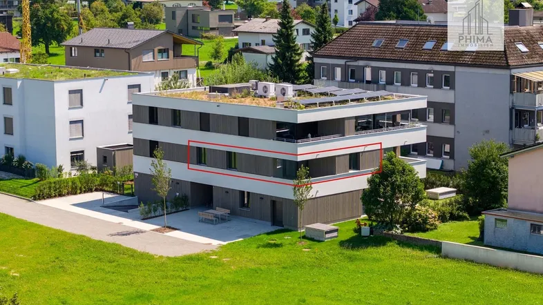 Luftaufnahme eines modernen Mehrfamilienhauses mit Flachdach und Solaranlage in grüner Umgebung.