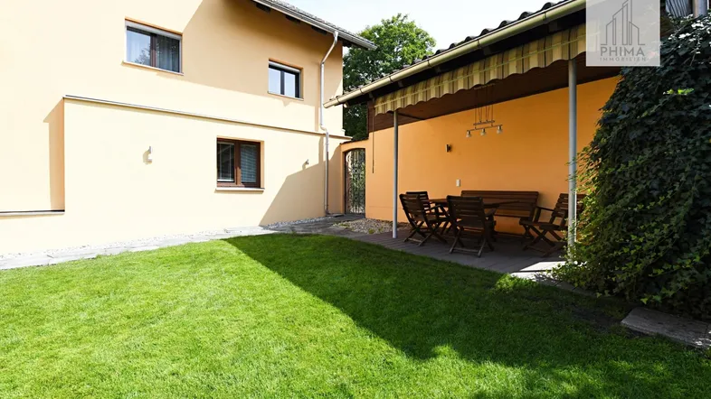 Überdachter Sitzbereich im Garten mit Rasenfläche und Hausfassade.